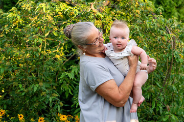 Grandmother holding smiling baby outdoors in lush garden