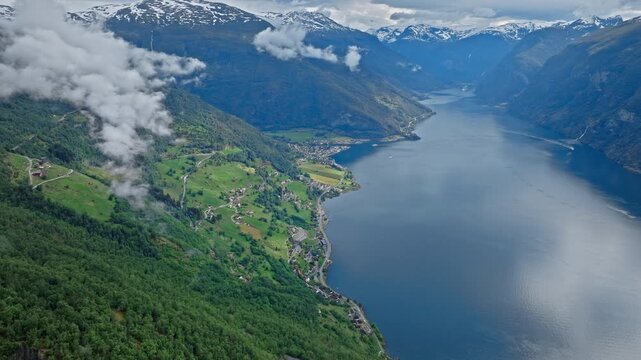 High aerial view of Aurlandsfjord and green valley farmland. Blue water curves through the landscape beneath low clouds in Norway.