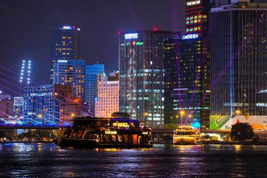 Night view of Bitexco Tower, colorful buildings, Bason bridge and Saigon river in Ho Chi Minh city, tourist boats and cruises on Saigon river