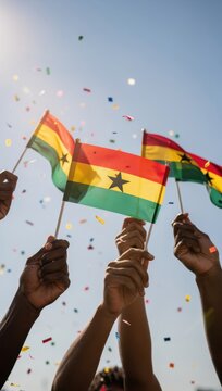 Hands raise Ghana flags with confetti during outdoor celebration