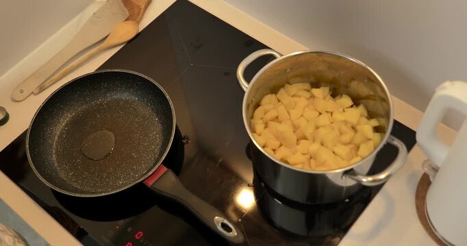 Close-up of hands frying boiled potato pieces in a pan on an induction cooktop