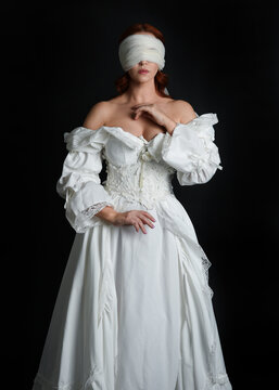 close up portrait beautiful female model wearing antique white historical ghost bride wedding dress gown, a veiled mask blindfold covering face. isolated figure on dark studio background, hand gesture