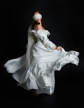 full length portrait beautiful female model wearing antique white historical ghost bride wedding dress gown, veiled mask blindfold covering face. isolated walking figure on dark studio background.