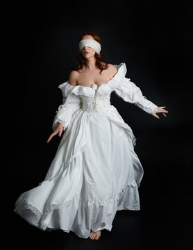 full length portrait beautiful female model wearing antique white historical ghost bride wedding dress gown, veiled mask blindfold covering face. isolated walking figure on dark studio background.