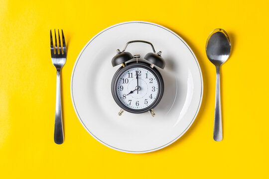 Empty plate with clock on a yellow background, intermittent fasting concept