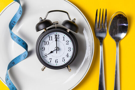 Empty plate with clock and measuring tape on a yellow background, intermittent fasting concept