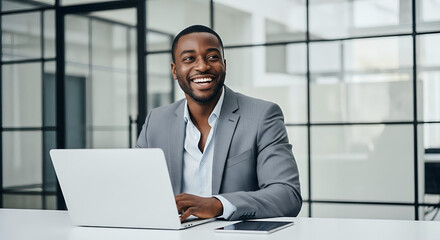 Smiling black businessman working on laptop in modern office with glass walls