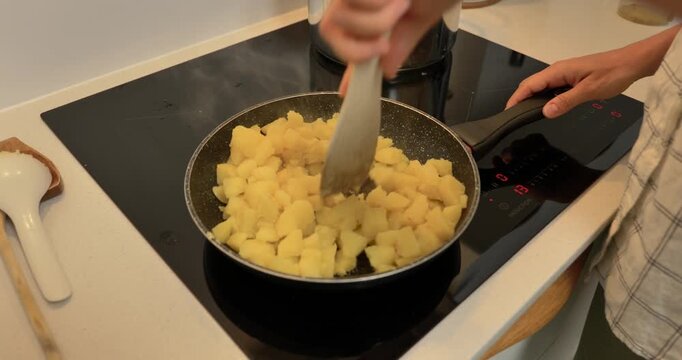 Close-up of hands frying boiled potato pieces in a pan on an induction cooktop