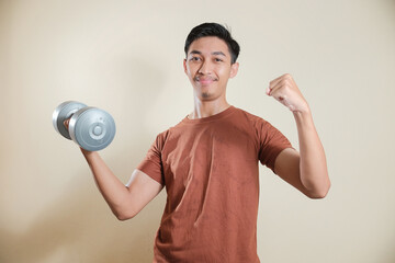 Smiling young Asian man holding a dumbbell and showing thumbs up gesture. Concept of fitness...