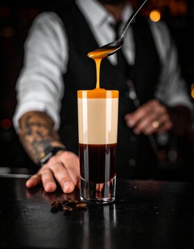C&oacute;ctel en capas con espuma y salsa de caramelo vertida сверху в барной атмосфере.
