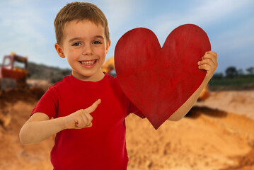 A young boy is holding a red heart and pointing to it
