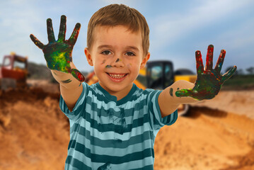 A young boy is holding his hands up in the air, with green and red paint on them