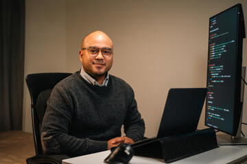 Male programmer wearing glasses works late at night with green code reflecting on his lenses focusing on software development coding and cybersecurity analysis.