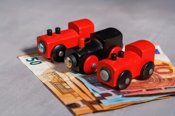 Fototapeta premium Model wooden train on bank bills with natural sunlight for transport cost inflation, travel debt and social mobility crisis themes.
