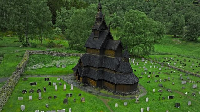 Aerial top-down view of Borgund Stave Church and graveyard, Norway. Dark wooden church stands at the center of a historic rural site.