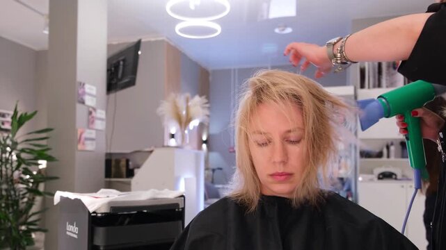 Moscow, Russia, 24.04.2025 Female hairdresser drying blonde womans highlights haircut with a blow dryer in beauty salon, hair treatment footage