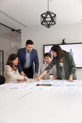 Four multiethnic colleagues teammates analyzing data in meeting room, take part in productive teamwork, data-driven decision-making, focused corporate planning in modern office. Analytics, forecasting