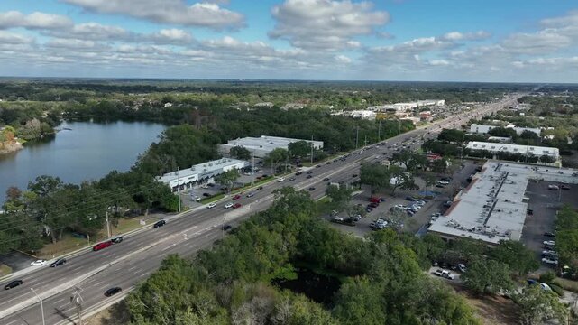 Aerial flyover suburb district of Brandon town, with traffic on highway beside large shopping mall center. Clouds at blue sky in summer season. Lake between scenic area of United States, Florida.