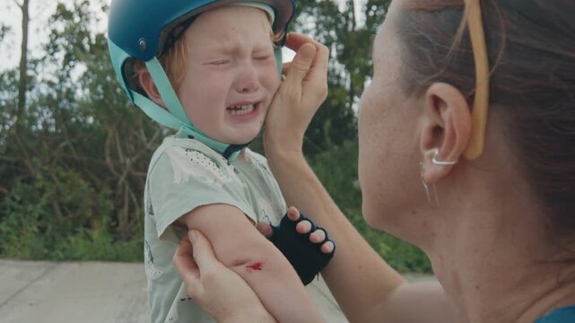 Toddler boy cries after falling and scratching his elbow. Boy cries and mother soothes him after incident on the rollerskate