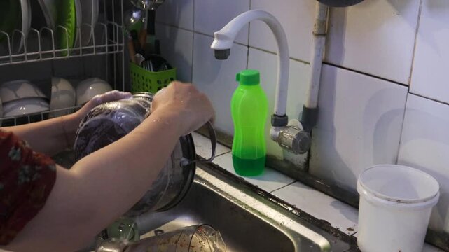 Washing dishes and cleaning utensils in the kitchen sink. A woman washes dishes in the kitchen at night while preparing for the next day.