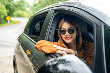 Naklejka premium Young beautiful asian women getting new car. she very happy and excited. Smiling female driving vehicle on the road on a bright day beautiful nature background.