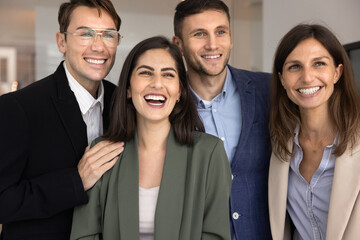 Four young and middle-aged multiethnic staff members laughing, look away with joyful expression, celebrate success, enjoy sales or career growth, showing team spirit and unity, having fun during break