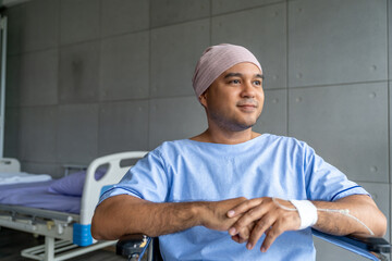 Obraz premium A male cancer patient in a wheelchair with an IV smiles with joy and hope showing strength and positivity during treatment. Man receiving IV therapy in a wheelchair appears happy and uplifted