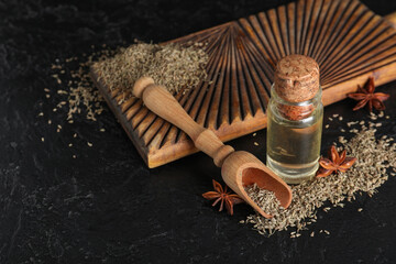 Wooden board with bottle of essential oil, anise stars, scoop and dried seeds on black grunge...