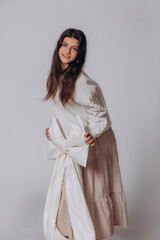 Fototapeta premium The model is a young beautiful brunette girl with a big white bow in a white sweater and skirt in the studio