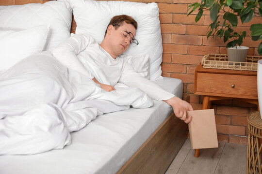 Young man fell asleep while reading book in bed at home