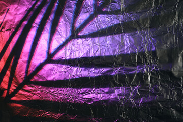 Palm leaf shadow on crumpled metallic foil with purple and pink neon light reflections