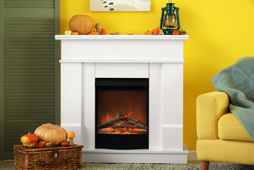 Naklejka premium Electric fireplace with pumpkins and lantern near yellow wall in living room