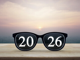 2026 white text with black eye glasses on wooden table over city tower and skyscraper at sunset, vintage style, Business vision happy new year 2026 concept