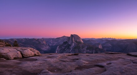 Obraz premium 高台から見下ろす広大な岩の台地と遠くに見える独特な形の雄大な山々 夕焼けの空は紫から鮮やかなオレンジへとドラマチックに変化し幻想的な光が風景全体を美しく染め上げる