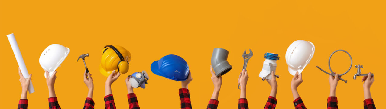 Many hands with hardhats and construction tools on yellow background