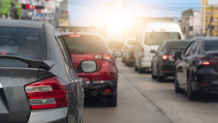 Rear side of cars on the concrete road stop by traffic red light control. Many cars on the road heading towards the goal of the trip. Town with light under sky for background.