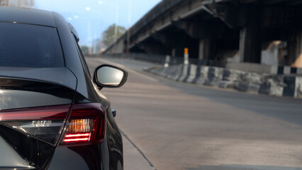 Fototapeta premium Rear side of luxury black car with turn on brake light. Driving on a clear road ready to turn right. The underpass is ahead. under blue sky at day time.