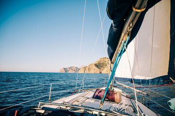 Fototapeta premium Sailboat Approaching Rocky Coastline Under Clear Skies