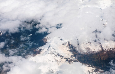 Aerial photo captures the majestic, snow-capped peak of Mount Rainier emerging from dense white clouds. Spectacular view of the active stratovolcano near Seattle, Washington