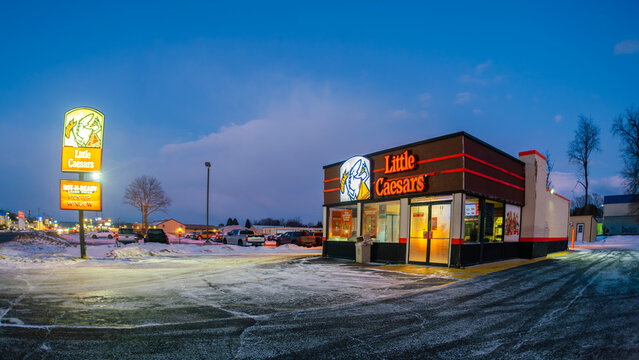 Whitesboro, NY - Jan 19, 2026: Little Caesars Enterprises Inc., a U.S. pizza chain founded in 1959, shown in fisheye with illuminated signage and HOT-N-READY pick-up window in a snowy suburban setting