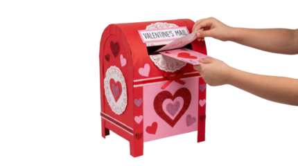 Handmade red and pink Valentine's mailbox decorated with glitter hearts receives greeting cards from a child's hands for a festive school classroom party or holiday celebration