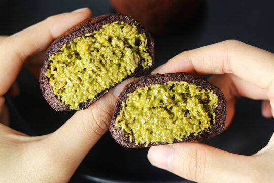 Hand holding the Dubai Chewy Cookie with the chewy outer layer opened to reveal the filling of pistachio and kataifi.