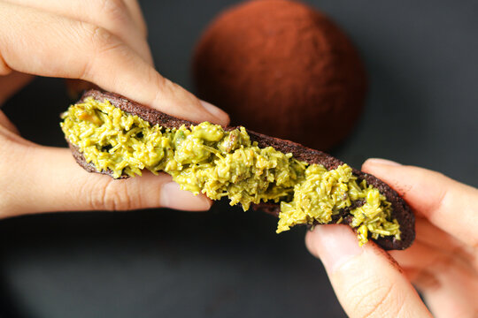 A hand stretching the Dubai Chewy Cookie with the chewy outer layer opened to reveal the filling of pistachio and kataifi.