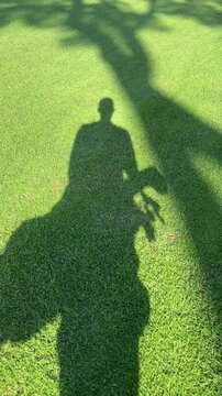 A man is standing on a green field with a golf club in his hand. The shadow of the man is cast on the grass, creating a sense of depth and dimension. The image evokes a feeling of leisure