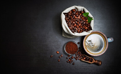 Coffee cup and coffee beans in canvas bag and ground powder on black wooden surface. Copy space. Flat lay.