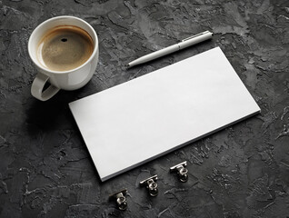 Blank envelope, pen and coffee cup on black plaster surface. Responsive design template.