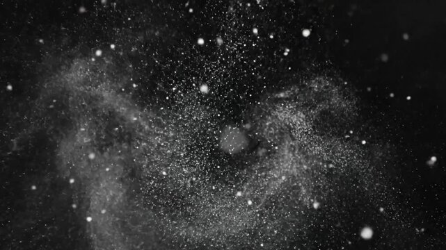 Abstract slow motion close up of a cloud of white particles floating against a black background