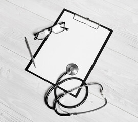 Doctor's medical supplies. Blank medical clipboard, stethoscope, glasses and pen on light wooden surface.