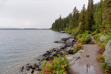 Wet hiking trail along the rocky shoreline of Jenny Lake on a cloudy day, Grand Teton National Park, Wyoming, USA © Eleseus