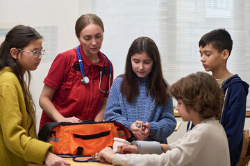 Caucasian female healthcare worker instructing group of multiethnic teenagers using medical equipment at table, teenagers observing and participating in hands-on learning activity